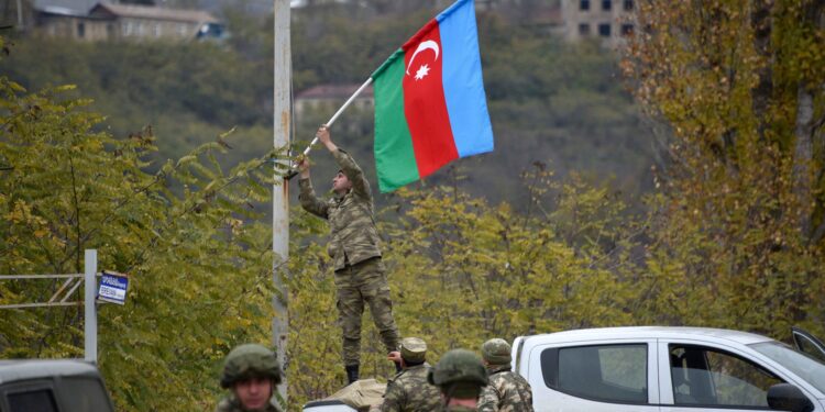 An Azerbaijani soldier fixes a national flag on a lamp post in the town of Lachin on December 1, 2020. - Azerbaijani soldiers and military trucks on December 1 rolled into the final district given up by Armenia in a peace deal that ended weeks of fighting over the disputed Nagorno-Karabakh region. (Photo by Karen MINASYAN / AFP)